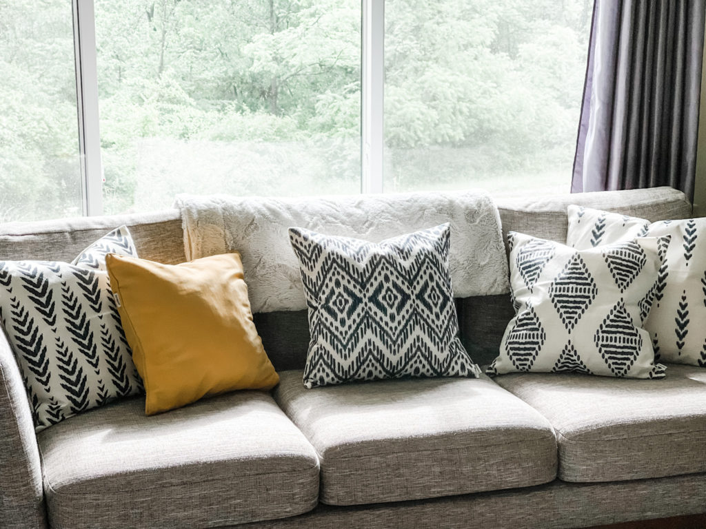 Boho and yellow pillows on a grey Mid-Century couch in a sunny living room
